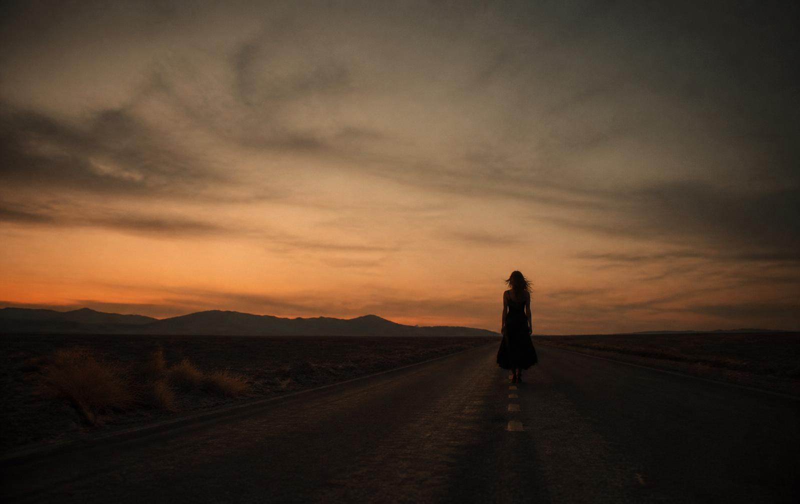 A lone figure on an empty desert road at dusk